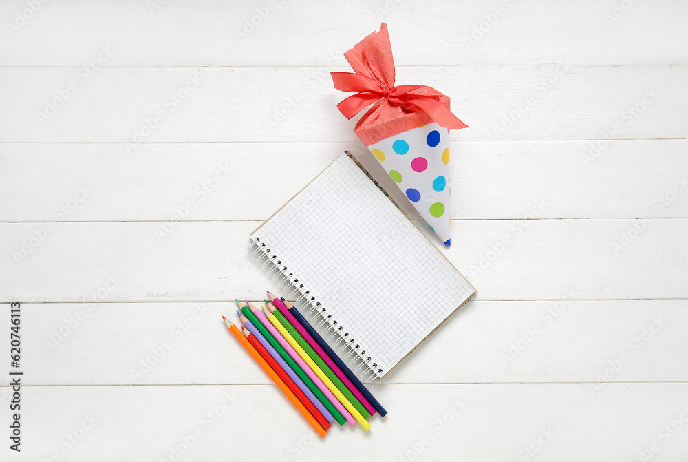 Blank notebook with red school cone and pencils on white wooden background