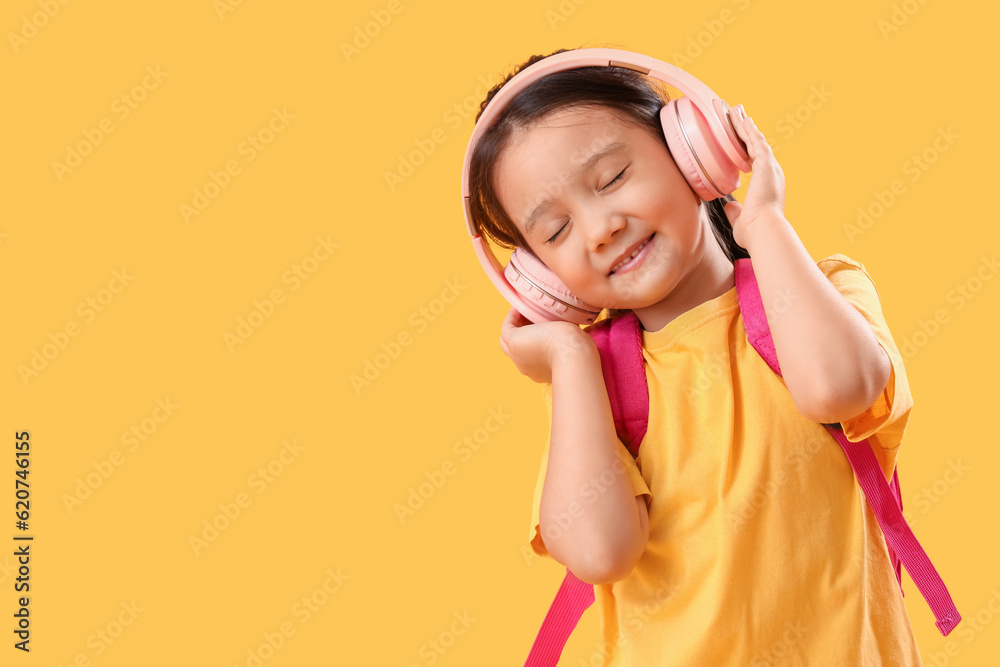 Little schoolgirl listening to music on yellow background