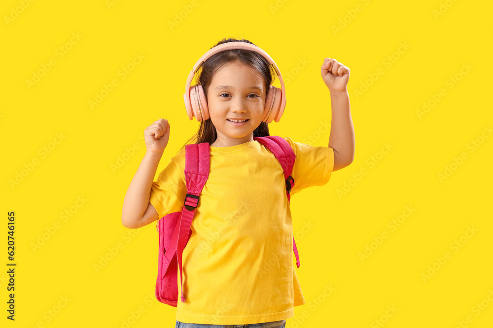 Little schoolgirl listening to music on yellow background