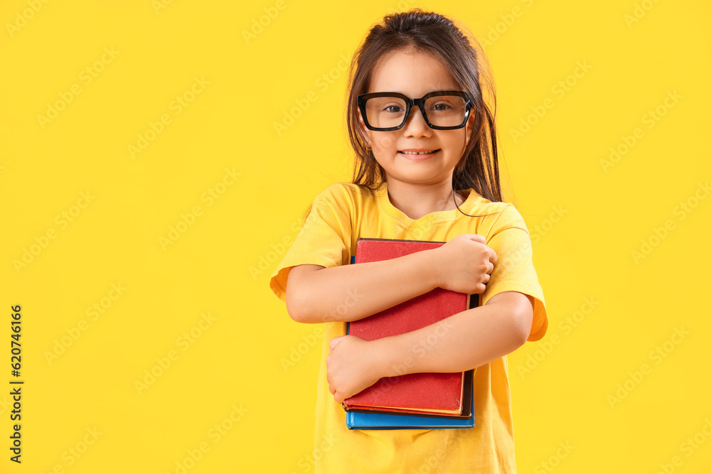 Little schoolgirl with books on yellow background