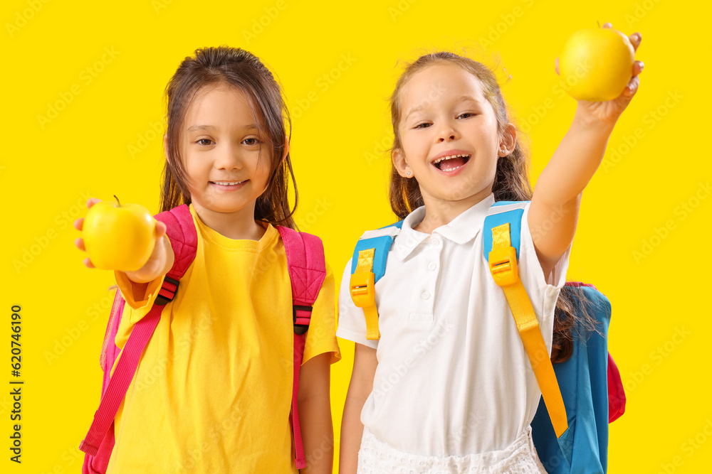 Little schoolgirls with apples on yellow background