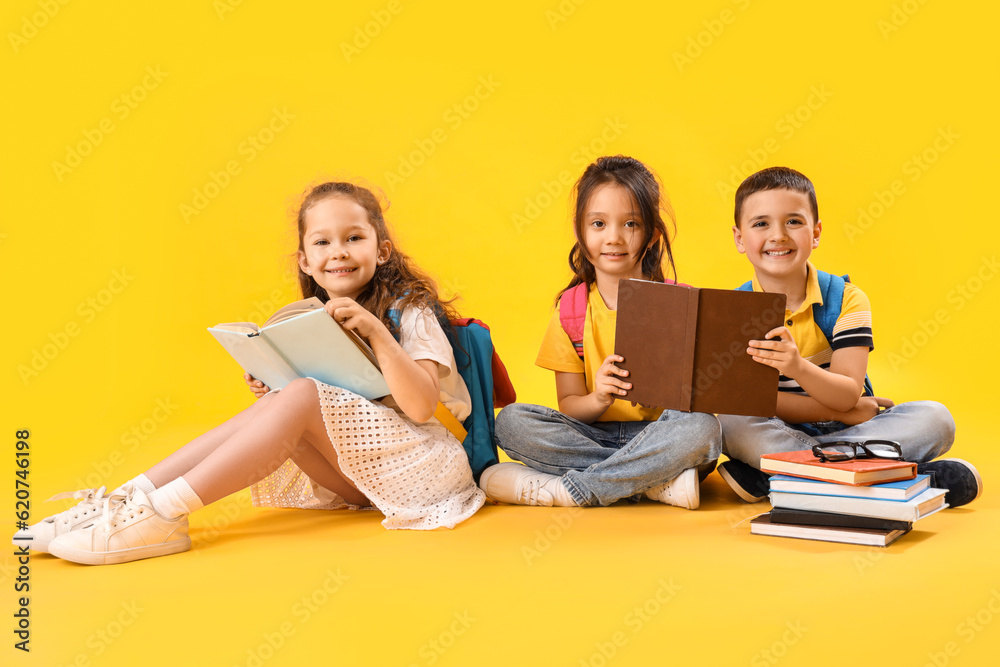 Little schoolchildren reading books on yellow background