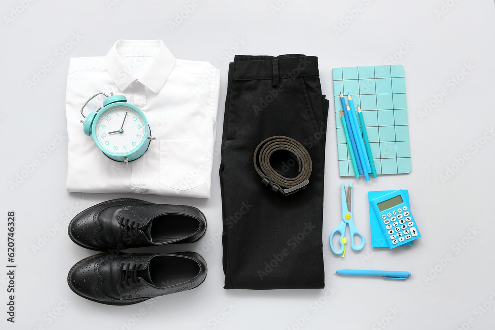 Stylish school uniform with alarm clock and stationery on grey background