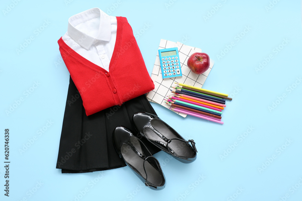 Stylish school uniform with fresh apple and stationery on blue background