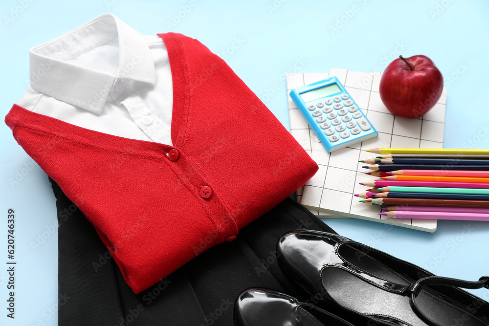 Stylish school uniform with fresh apple and stationery on blue background