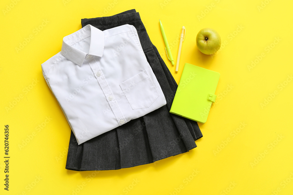 Stylish school uniform with fresh apple and stationery on yellow background