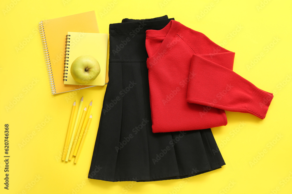 Stylish school uniform with fresh apple and stationery on yellow background