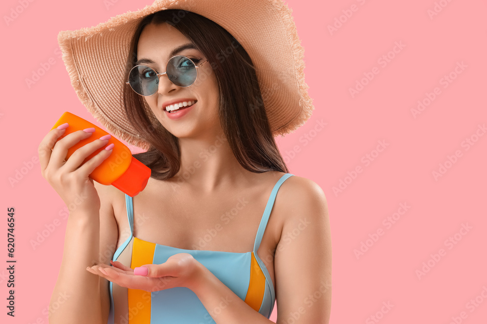 Young woman applying sunscreen cream on pink background