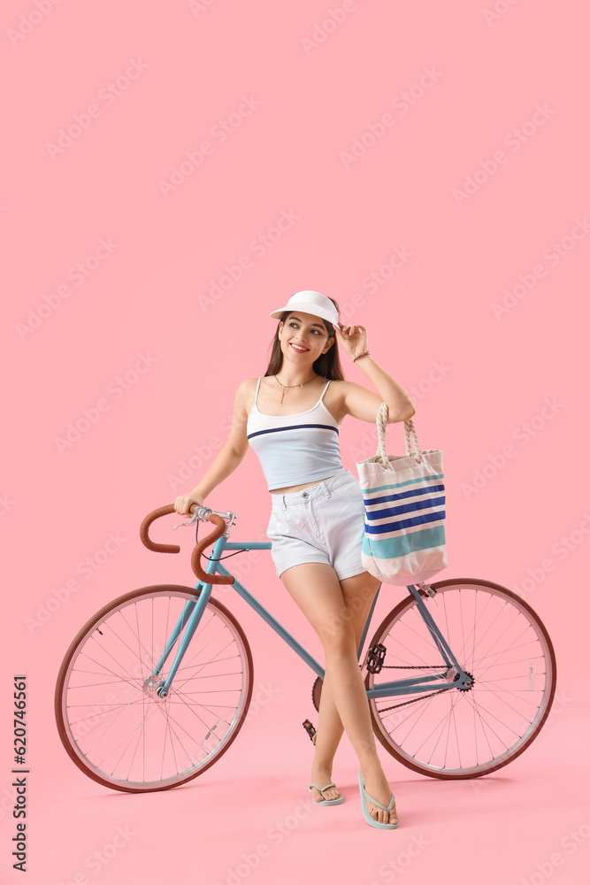 Young woman with bag and bicycle on pink background