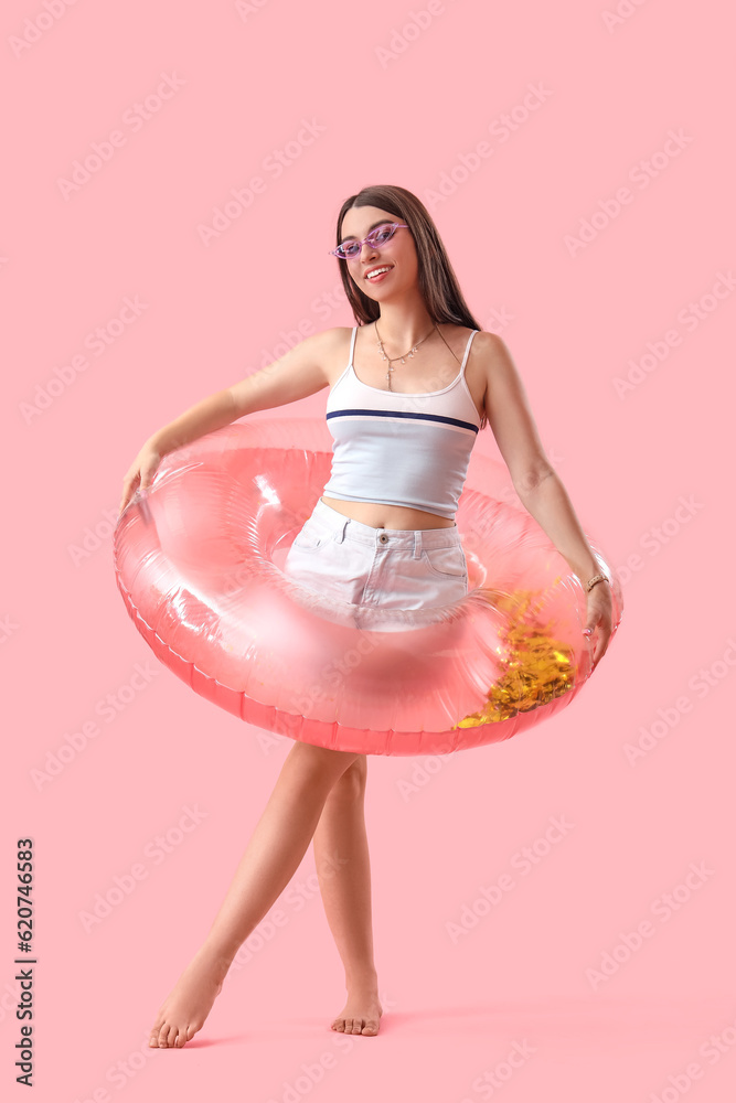 Young woman with inflatable ring on pink background