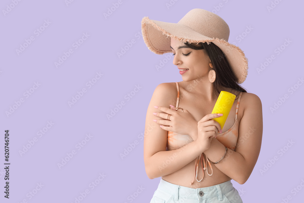 Young woman with sunscreen cream on lilac background