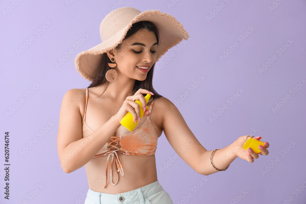 Young woman applying sunscreen cream on lilac background