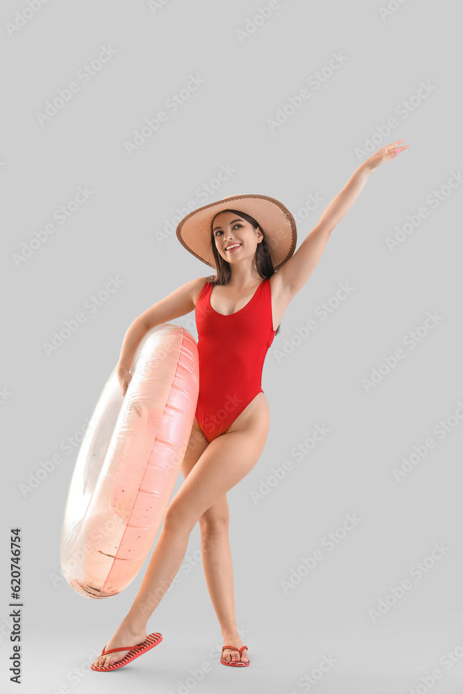 Young woman in swimsuit with inflatable ring on light background