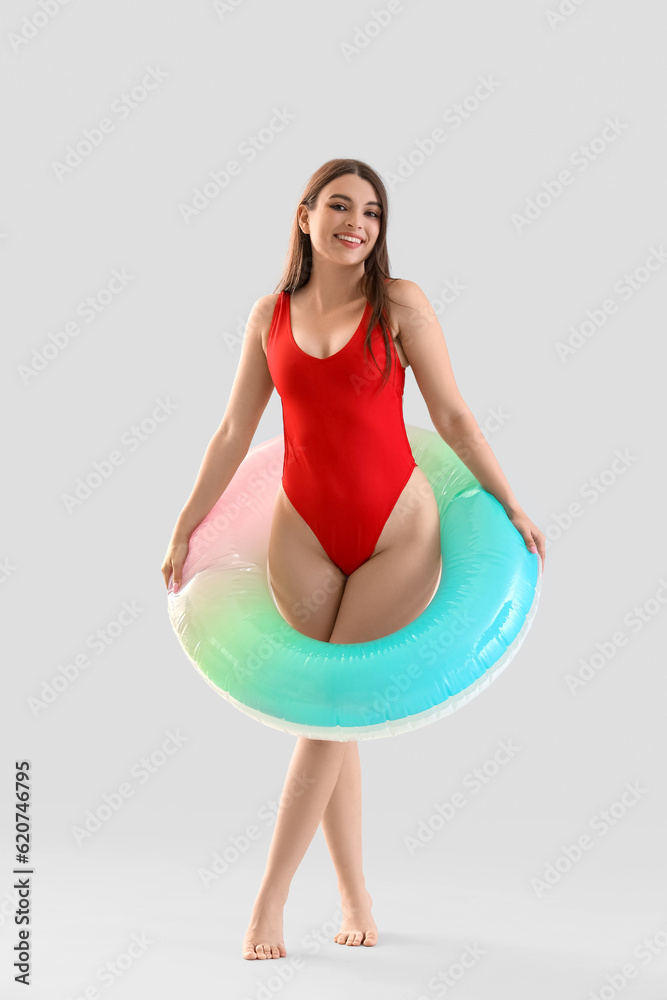 Young woman in swimsuit with inflatable ring on light background