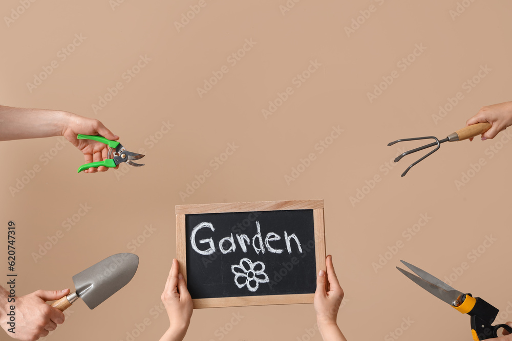 People holding chalkboard with word GARDEN and tools on beige background