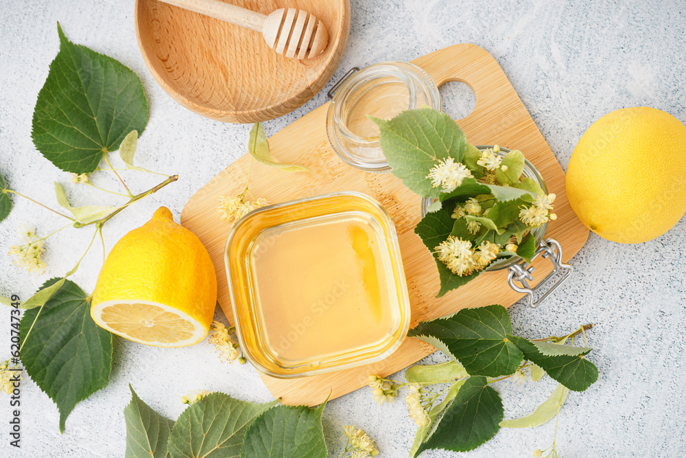 Wooden board with glass bowl of linden honey and lemon on white background