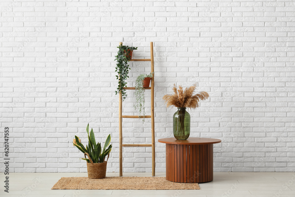 Wooden ladder, table and houseplants near white brick wall in room