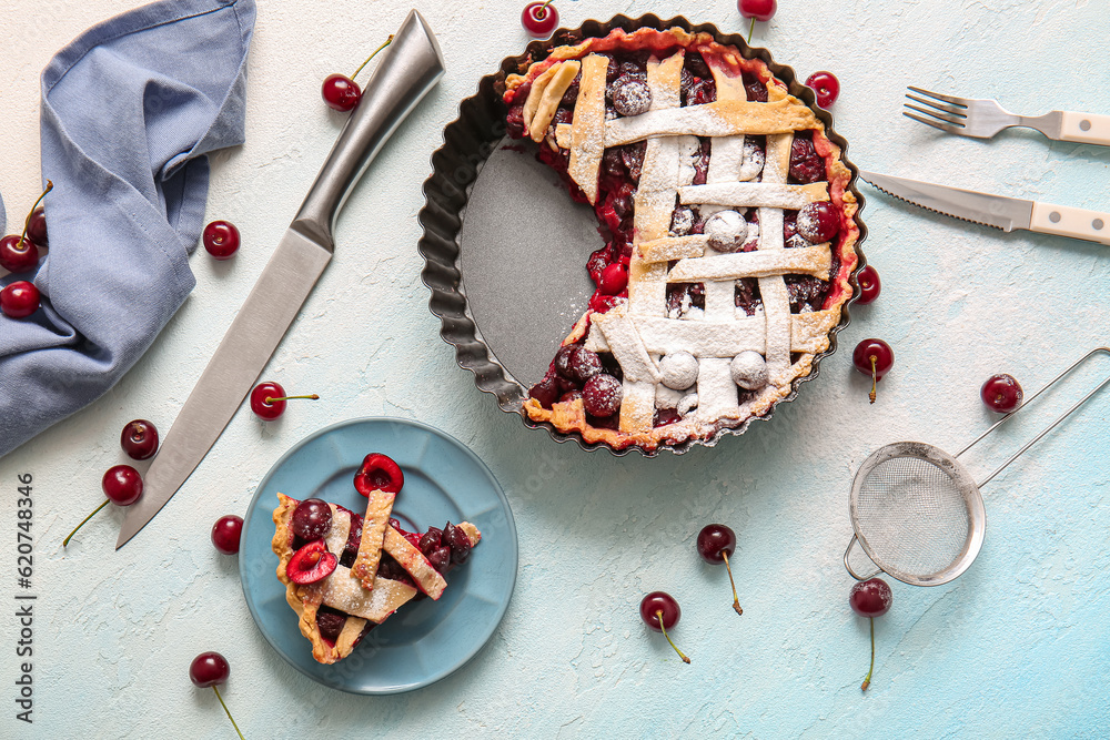 Baking dish with tasty cherry pie and plate of piece on blue background