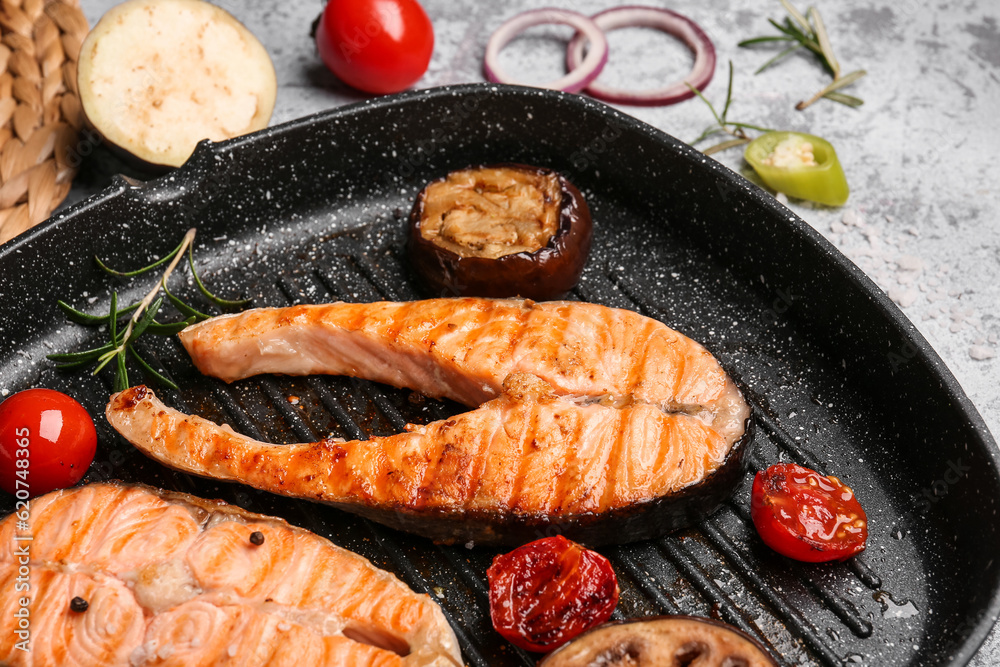 Frying pan with tasty grilled salmon steaks and vegetables on grey background