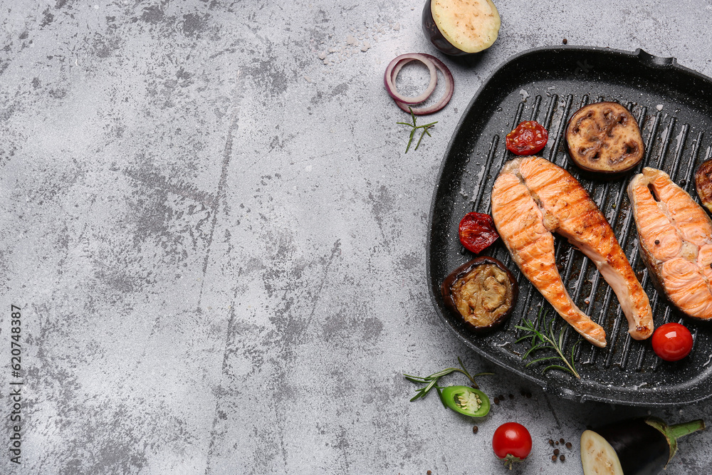 Frying pan with tasty grilled salmon steaks and vegetables on grey background