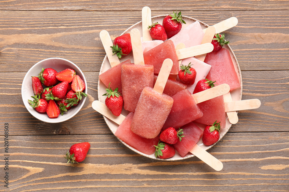 Plate with sweet strawberry ice-cream popsicles and bowl of berries on wooden background