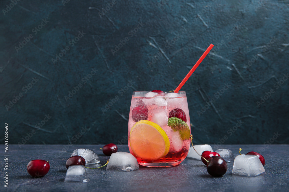 Glass of tasty cherry lemonade with lime and ice cubes on dark background