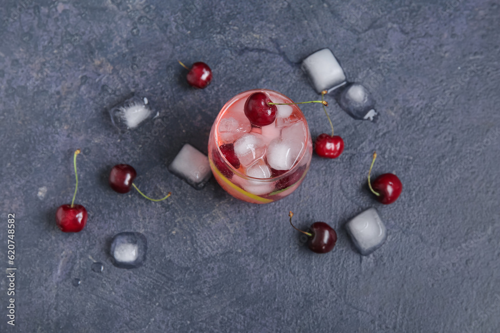 Glass of tasty cherry lemonade and ice cubes on dark background