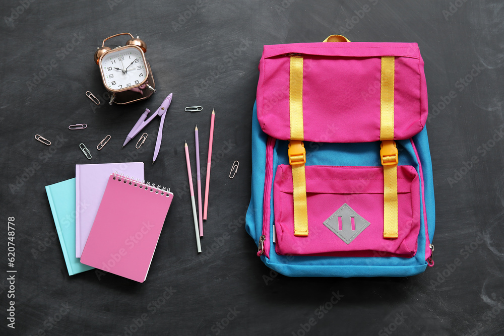 Colorful school backpack with notebooks, alarm clock and pencils on black background