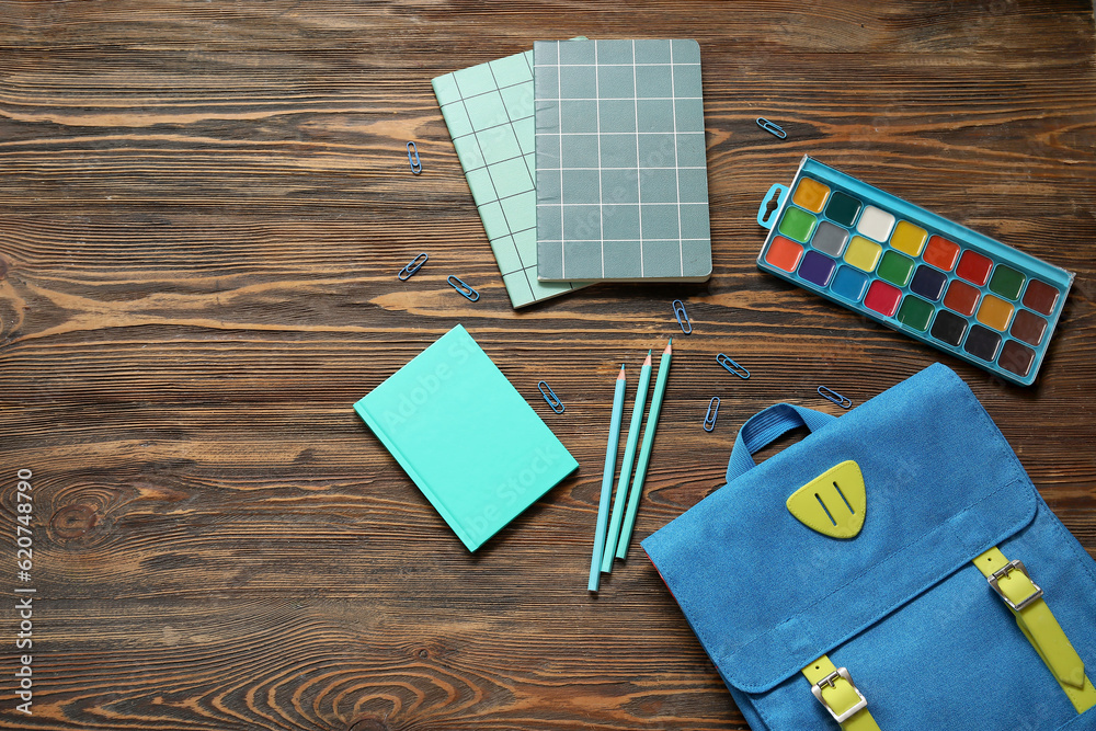 Blue school backpack with notebooks, watercolors and pencils on brown wooden background