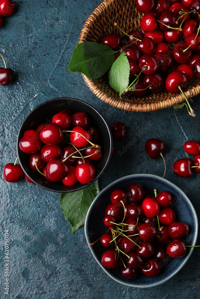 Bowls with sweet cherries on blue background