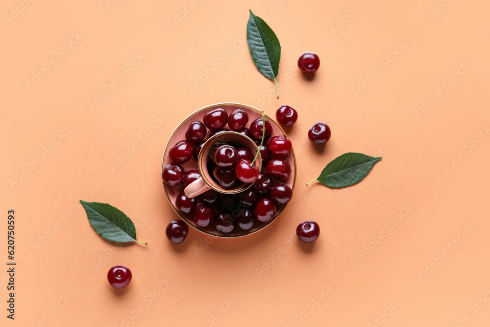 Cup and plate with sweet cherries on orange background