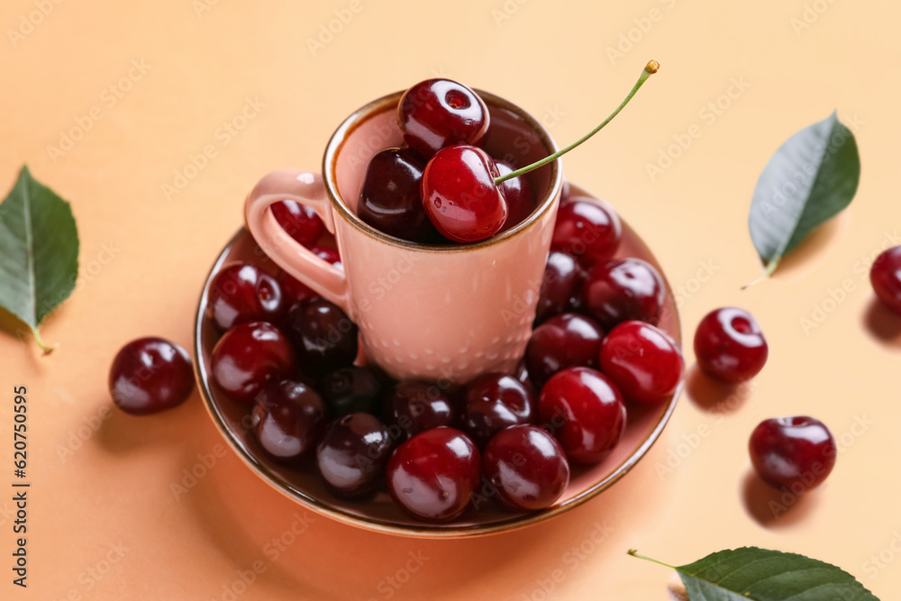 Cup and plate with sweet cherries on orange background