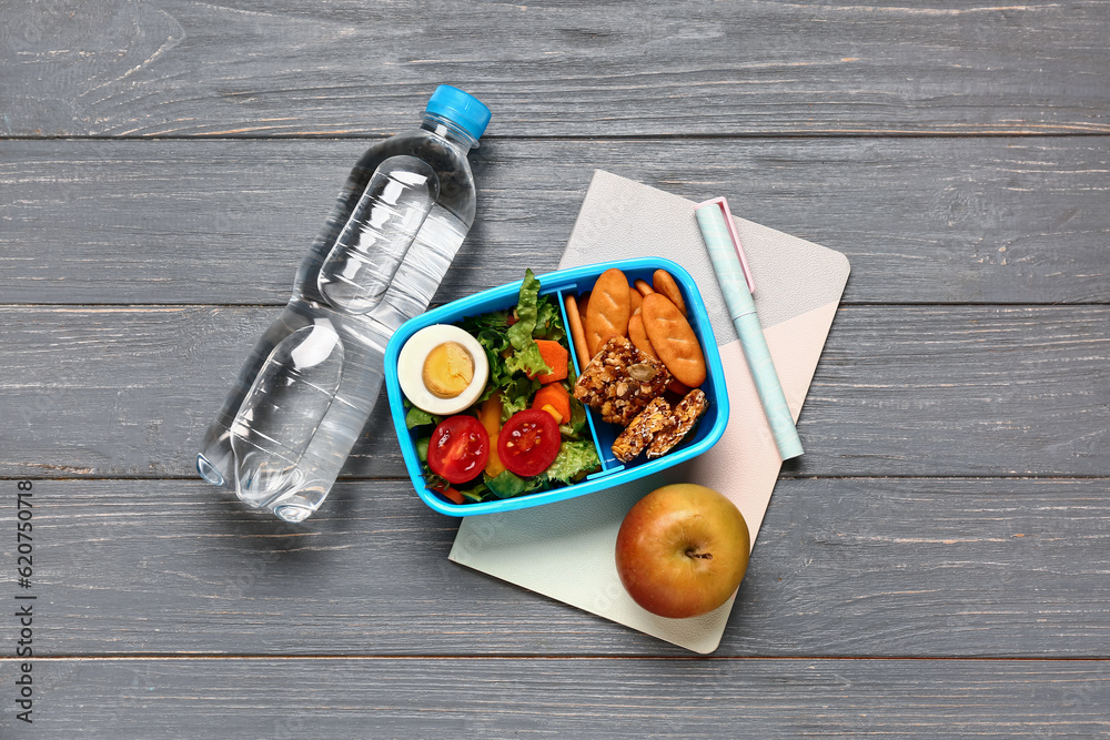 Bottle of water, stationery and lunchbox with tasty food on grey wooden background