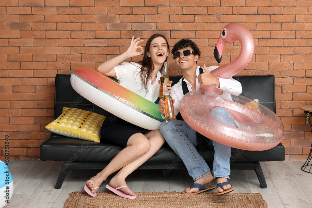 Young couple with beer and swim rings ready for summer vacation in office