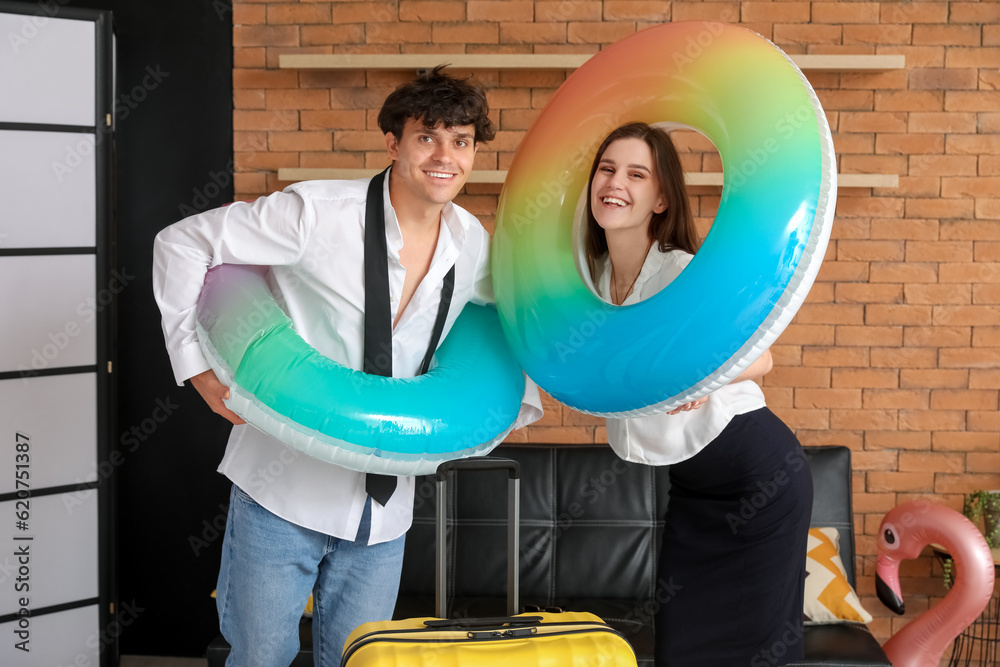 Young couple with swim rings and suitcase ready for summer vacation in office