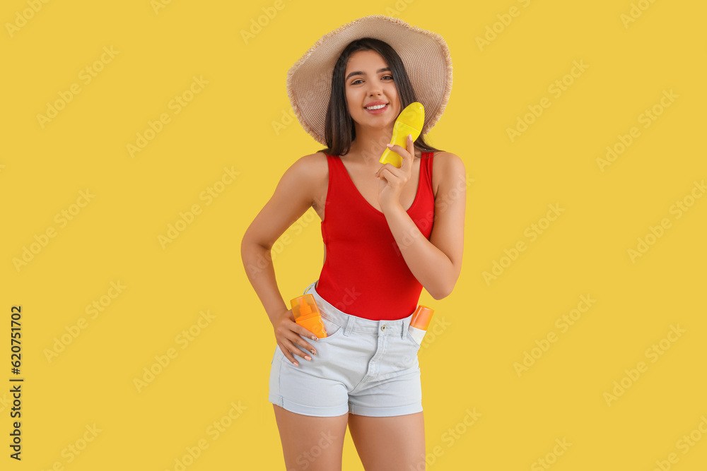 Beautiful young woman with bottles of sunscreen cream on yellow background