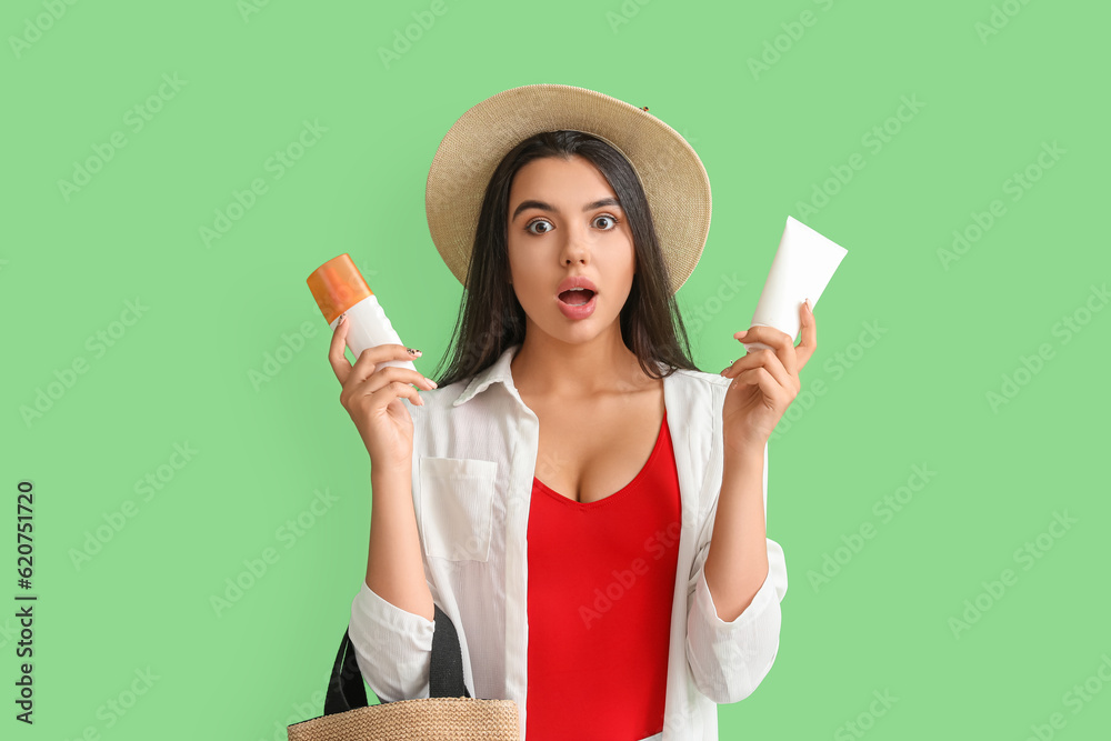 Surprised young woman with bottles of sunscreen cream on green background