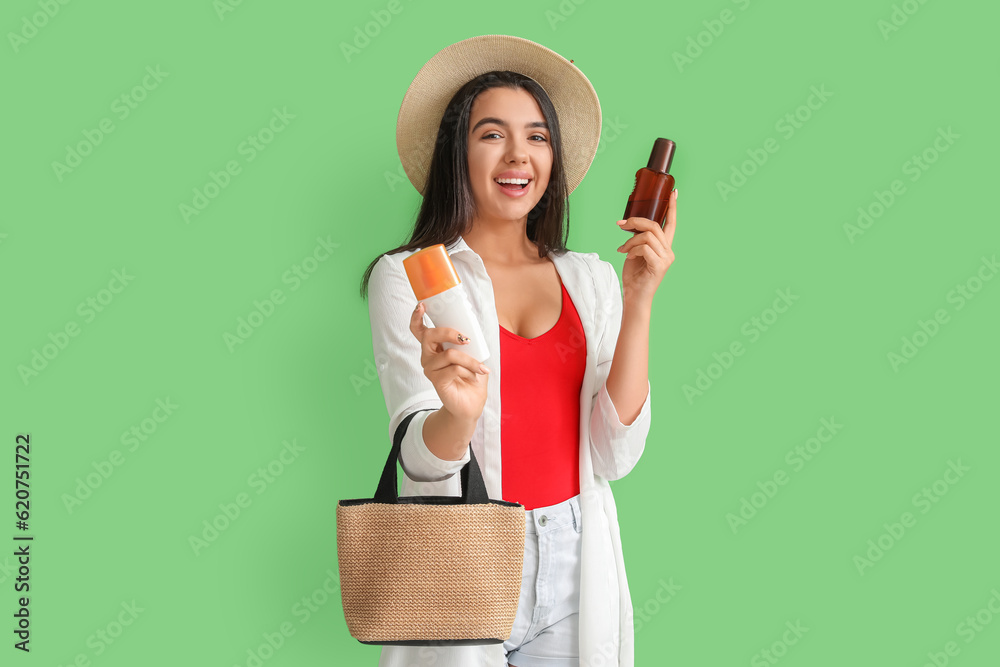 Beautiful young woman with bottles of sunscreen cream on green background