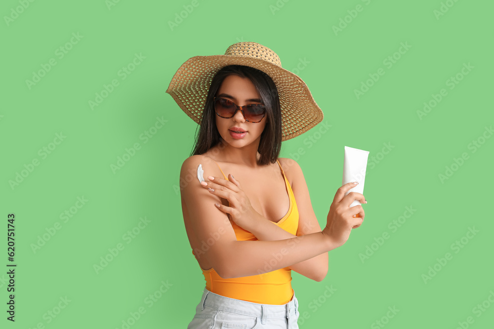 Beautiful young woman applying sunscreen cream on green background