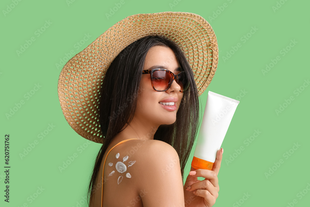 Beautiful young woman with sun made of sunscreen cream on green background