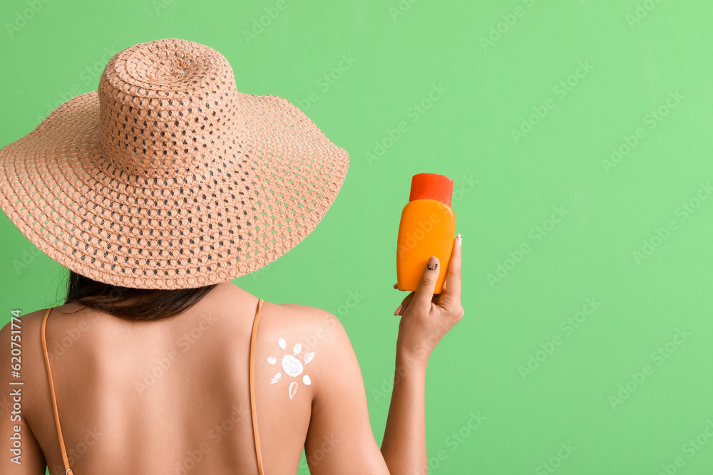 Beautiful young woman with sun made of sunscreen cream on green background, back view