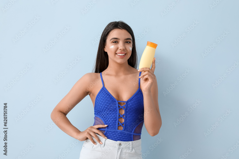 Beautiful young woman with sunscreen cream on light background