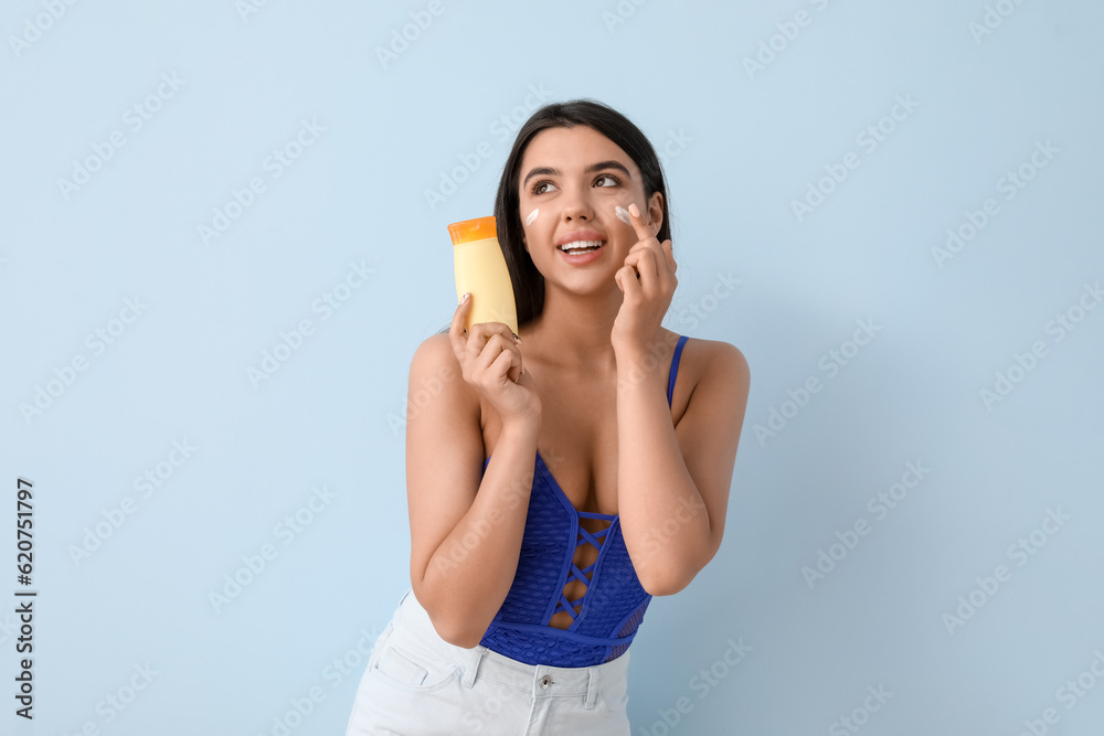 Beautiful young woman applying sunscreen cream on light background