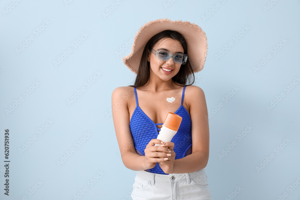 Beautiful young woman with heart made of sunscreen cream on light background