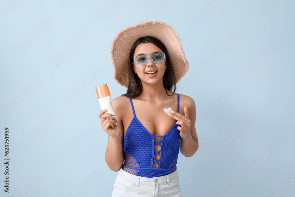 Beautiful young woman with heart made of sunscreen cream on light background