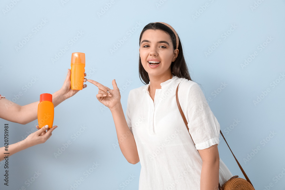 Beautiful young woman choosing sunscreen cream on light background