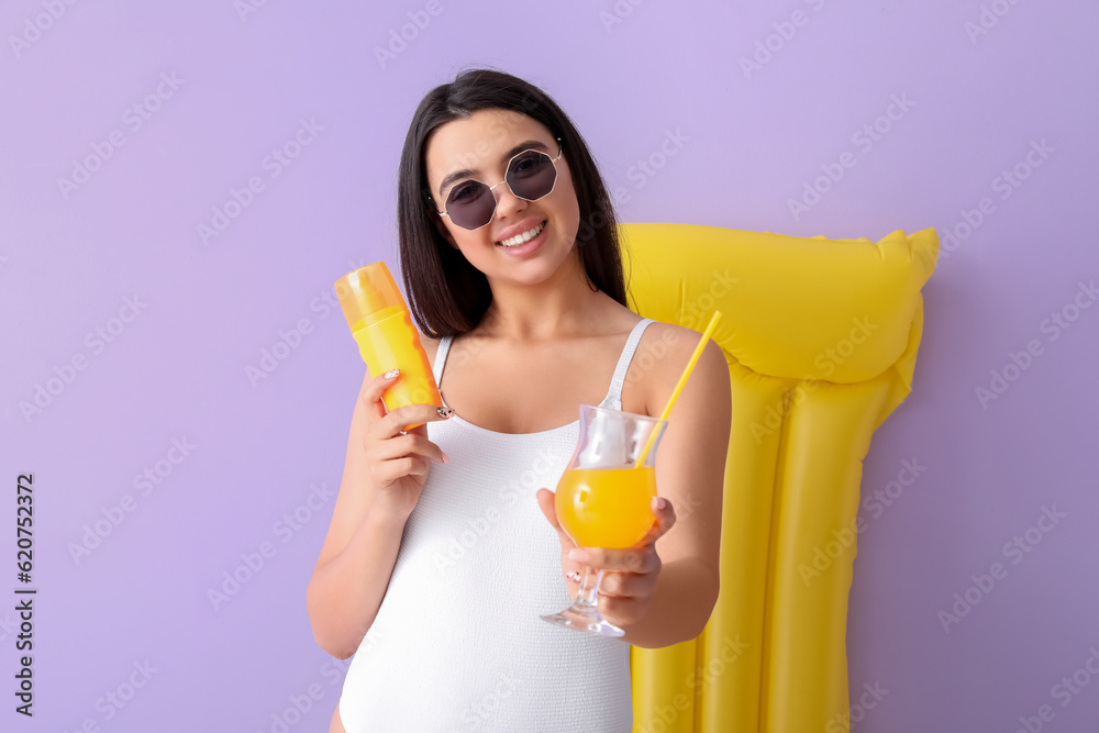 Beautiful woman with sunscreen cream, cocktail and swim mattress on lilac background