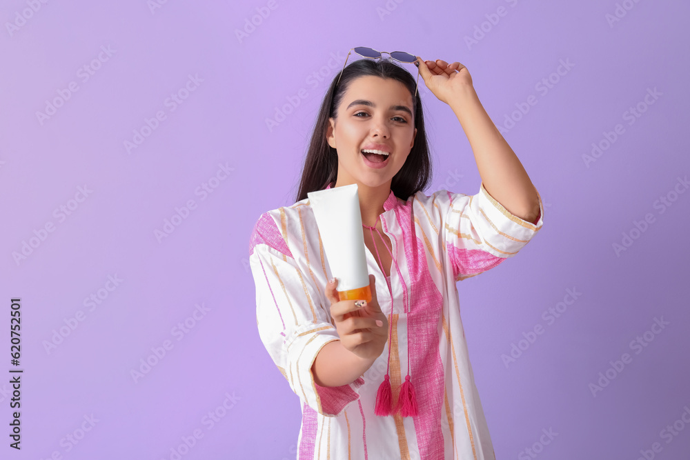 Beautiful young woman with sunscreen cream on lilac background