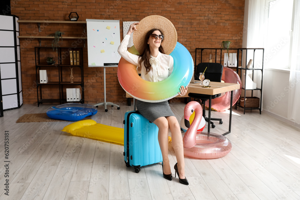 Young businesswoman with swim ring and suitcase ready for summer vacation in office