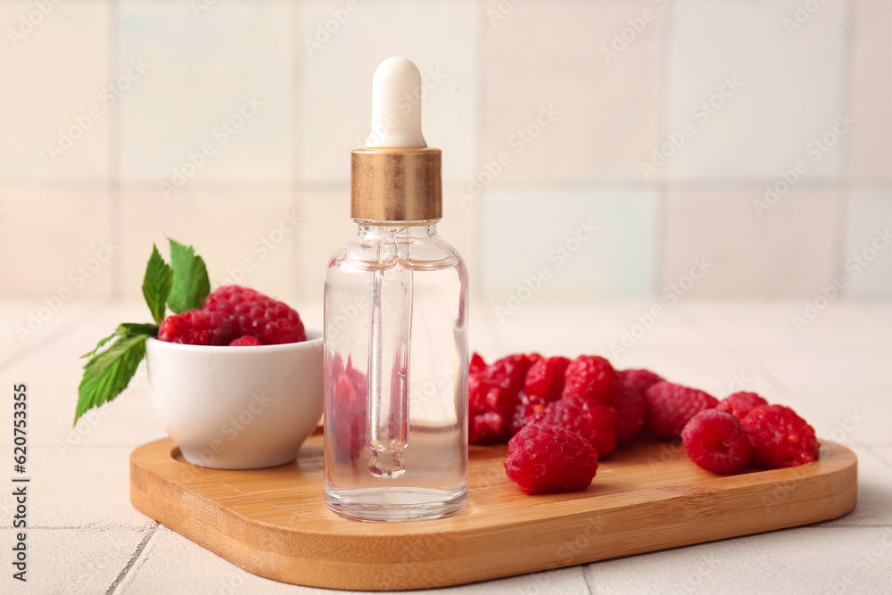 Wooden board with bottle of cosmetic raspberry oil on white tile background